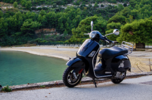 Black scooter parked by the beach with a scenic background of trees and water